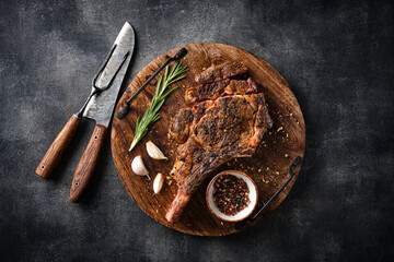 Freshly grilled Tomahawk steak on a wooden cutting board, BBQ food, top view, grey background.