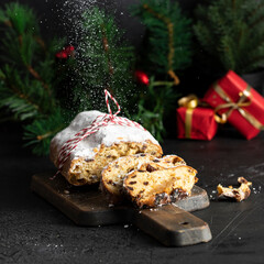 Traditional GermanChristmas cake , Stollen on cut board with red Christmas decoration snow and gifts. Christmas food background.