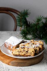 Stollen slices with dried fruit and marzipan coated with powdered icing sugar in the white plate on the table with Christmas tree branch