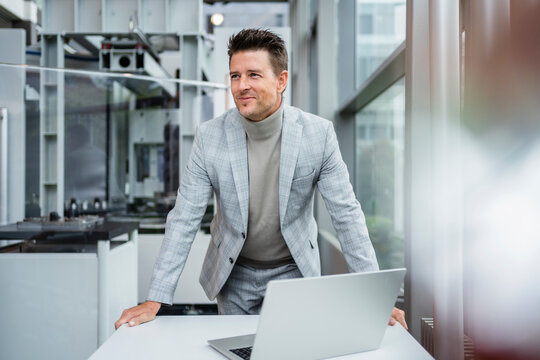 Smiling businessman with laptop at desk in industry