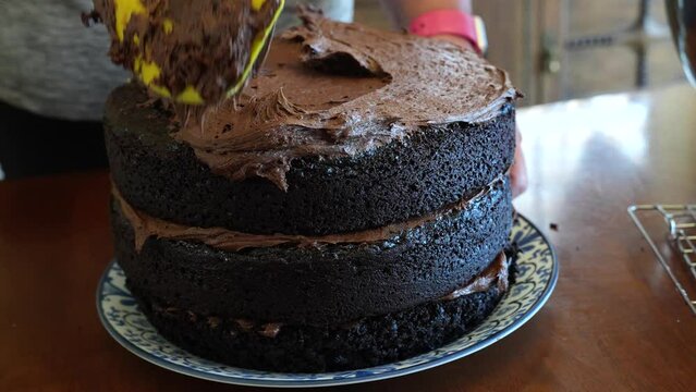 Spreading chocolate frosting on top of a triple-layer cake - CHOCOLATE CAKE SERIES