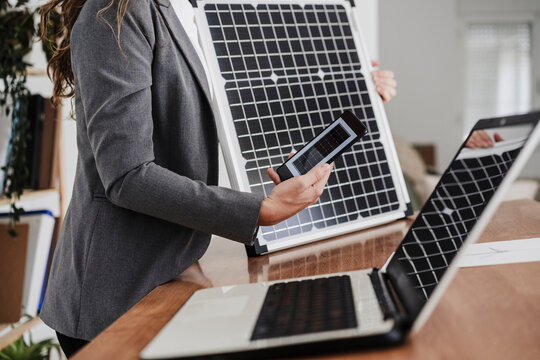 Modern businesswoman with smartphone using portable solar module in office - Powered by Adobe