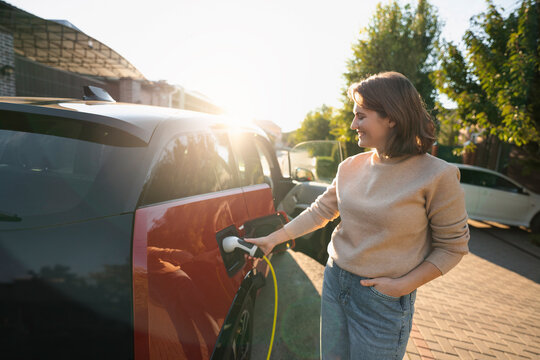 Happy woman charging electric car at roadside on sunny day - Powered by Adobe