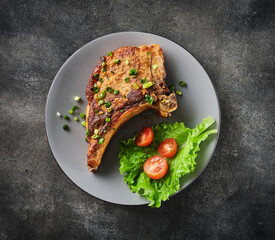 Grilled pork chop on grey plate sprinkled with green onions with salad and cherry tomatoes.
