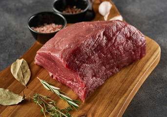 Piece of raw rump steak prepared with spices on wooden board over grey background.