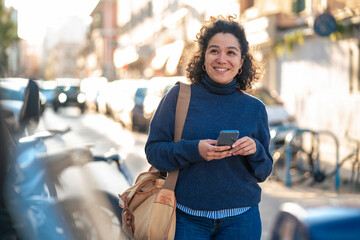 Smiling woman with smart phone and bag walking at street