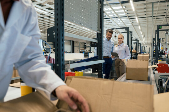 Businesswoman by businessman with engineer working in foreground at factory
