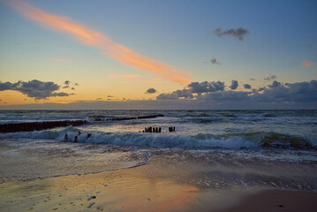 Panoramic view of sea beach with splashing waves against dramatic cloudy sky. Baltic sea coastline at sunset