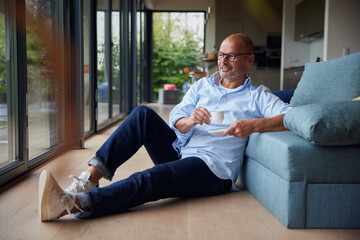 Smiling man with coffee cup sitting by sofa at home
