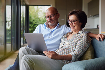 Happy senior woman with man using laptop at home