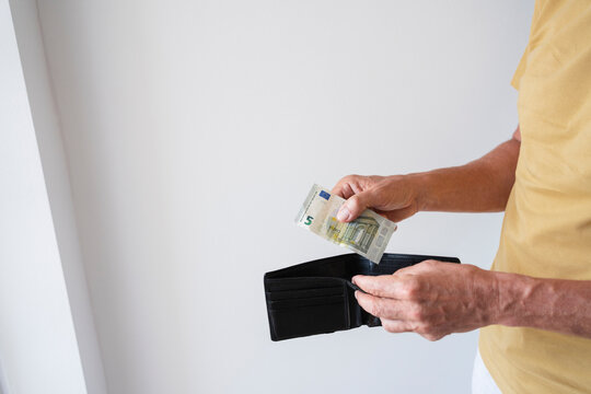 Hands of man holding wallet with banknote standing by wall at home