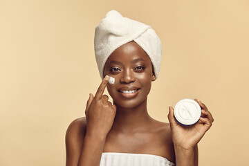 Positive brown skinned girl applying cream to her face.
