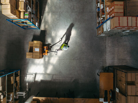 Overhead shot of a warehouse worker pulling a pallet truck while moving goods in a distribution center 