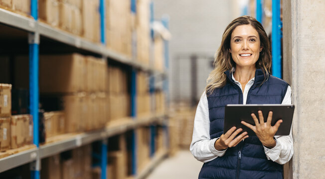 Female warehouse manager smiling at the camera while holding a digital tablet