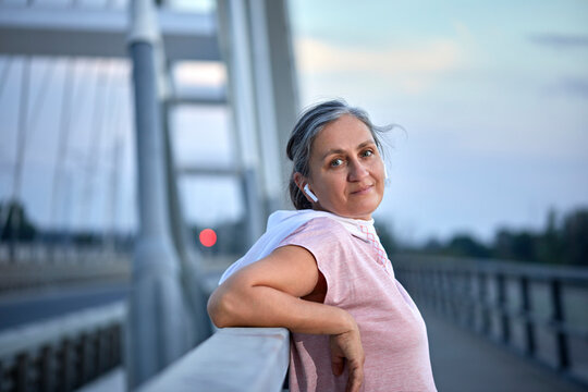 Smiling woman with wireless in-ear headphones leaning on railing