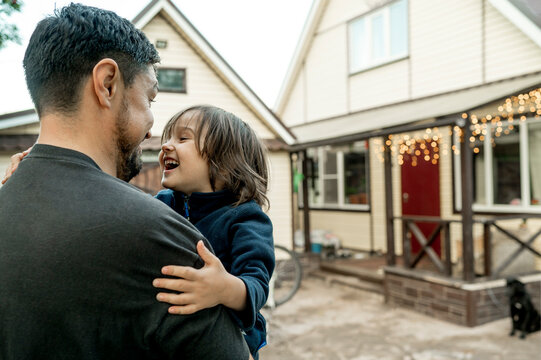 Happy Father Carrying Son In Front Of House