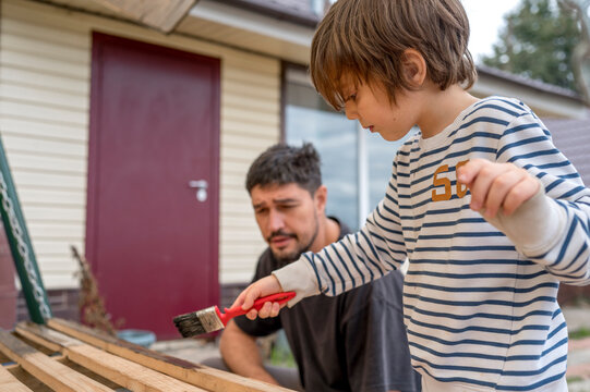 Father looking at son painting wooden swing in front of house
