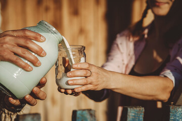Hands of man pouring milk into woman's glass jar on sunny day