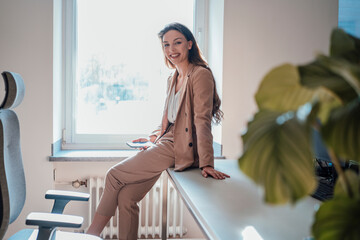 Happy young woman with smart phone sitting on desk at home office