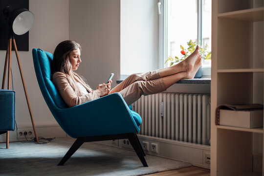 Businesswoman with feet up using smart phone on chair at home
