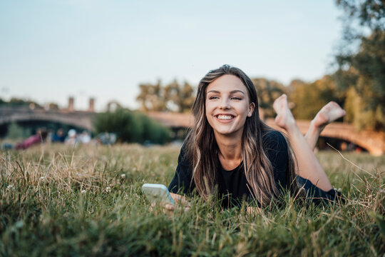 Happy Woman With Smart Phone Lying On Grass At Park