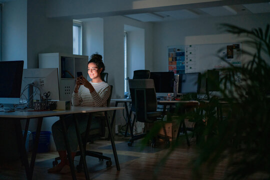 Smiling woman using smart phone in dark office