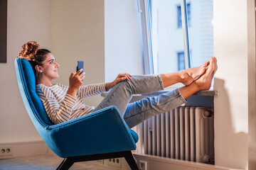Thoughtful woman with mobile phone relaxing on chair at home