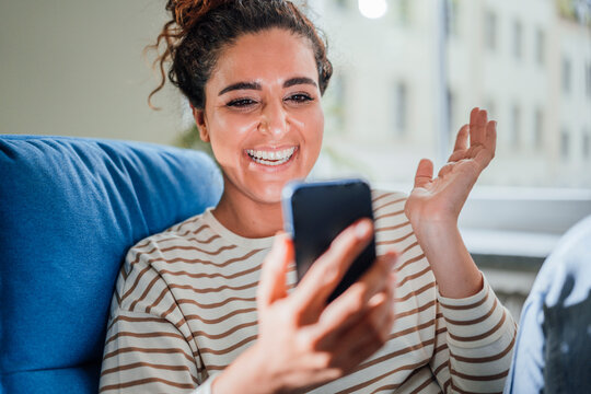 Happy Woman Gesturing On Talking Video Call Through Smart Phone At Home