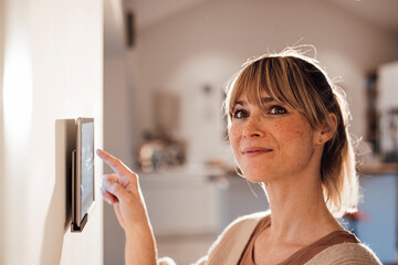 Smiling woman using smart home app on tablet at home