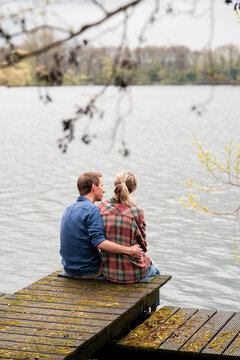 Man with arm around woman sitting on jetty at lake