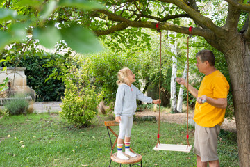 Granddaughter helping grandfather making swing with rope in garden