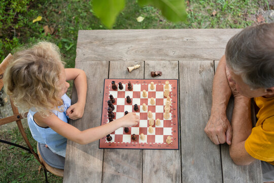 Granddaughter and grandfather playing chessboard in garden