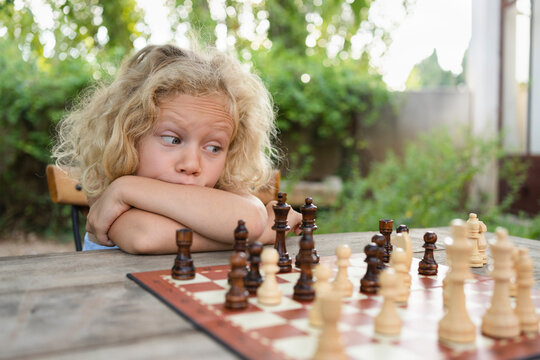 Thoughtful Girl With Blond Hair Looking At Chessboard On Table