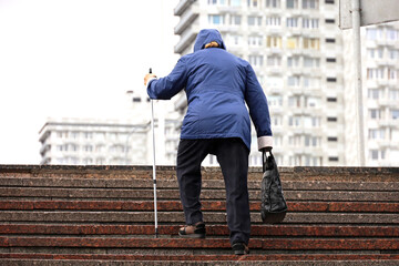 Old woman with walking cane climbing stairs on city street. Concept for disability, limping adult, diseases of the spine - obrazy, fototapety, plakaty