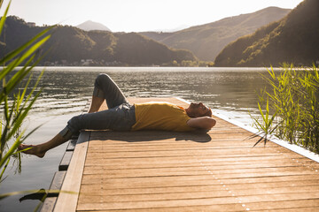 Mature man relaxing on jetty over lake by mountains
