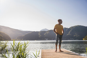 Smiling man with knit hat and hands in pockets on jetty over lake