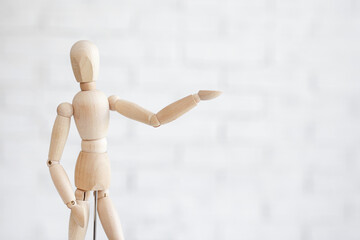 close up of wooden human figure pointing at something over white brick wall background