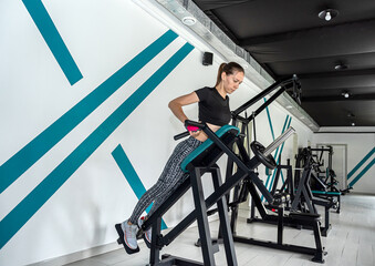young sporty girl in leggings and a top is trying many new x exercises on different simulators.