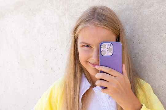 Teenage girl holding mobile phone's camera in front of her eye