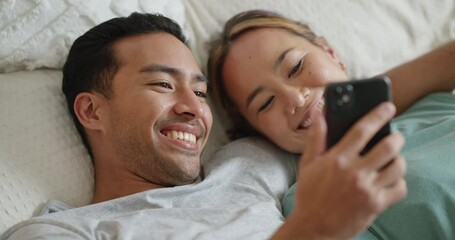 Phone, social media and communication with a couple in bed to relax, laughing and relaxing in a bedroom of a home together. Diversity, internet and mobile with a man and woman looking at a funny meme - Powered by Adobe