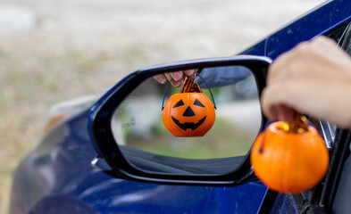 smiling plastic halloween pumpkin mini small pumpkin in reflection rear view retractable lateral mirror.woman hand holding pumpkin bucket handle.trick or treat holiday, car auto vehicle vehicle part