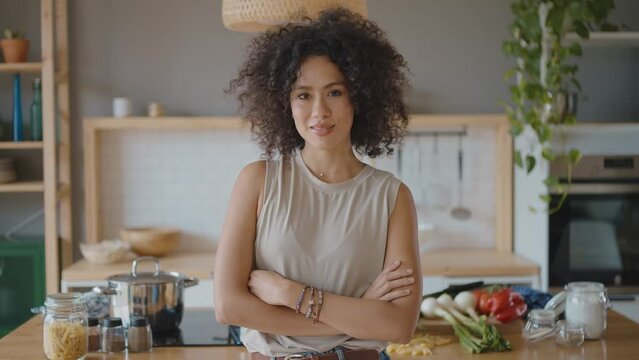 Happy young latin woman smiling at camera in her kitchen. Concept about lifestyle, carefee and successful women