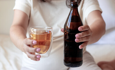 pregnant woman holding beer bottle and double wall glass fulfilled with beverage.overstretched ahead hands.pregnancy and alcohol expecting female awaiting childbirth drinking beer.bedroom interior