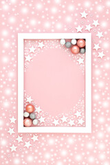 Pink Christmas background border with snow, stars, tree ball bauble decorations. Festive pastel design for holiday season and New Year with white frame.