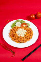 Spicy noodles with topping and vegetables on red background