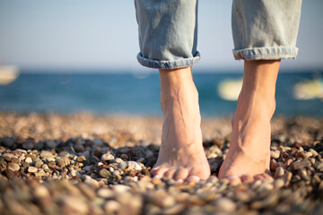 Barefoot massage grounding healthy step on a stone beach seaside. Relaxing vacation photo women legs in jeans banner selective focus macro narrow grip.