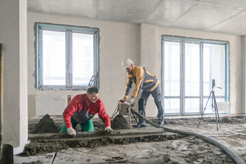 Workers in work clothes are doing their job, leveling the floor and pouring concrete