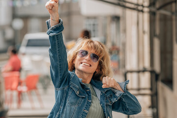 happy middle aged woman with raised arms and victory gesture on the street