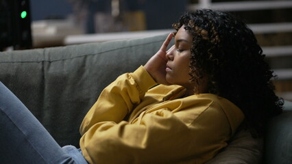 One upset young black woman feeling frustration. An anxious African American girl laid on sofa in living room at night