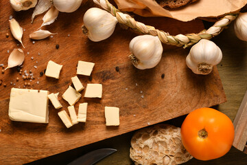 Fototapeta na wymiar still life of food in a rural style on a dark wood background, sliced cheese, garlic, onion and tomatoes, concept of healthy food